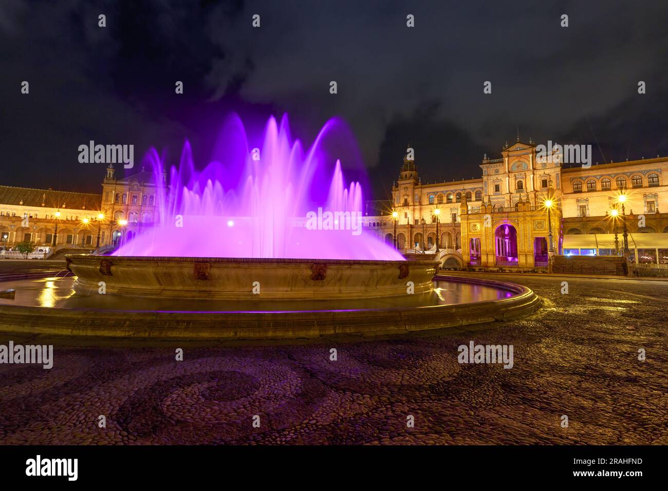 Quando la notte abbraccia Plaza de Espana a Siviglia, la fontana diventa uno spettacolo affascinante, inondato di luci radianti. L'acqua a cascata, colorata Foto Stock