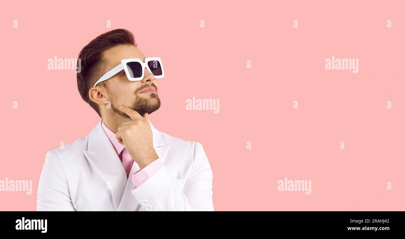 Uomo in costume e occhiali da sole che pensa a qualcosa su sfondo rosa con striscione Foto Stock