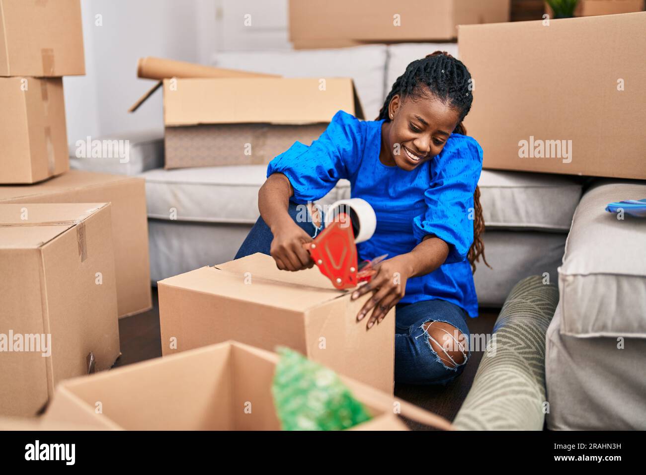 Donna afroamericana sorridente sicuro imballaggio scatola di cartone in nuova casa Foto Stock