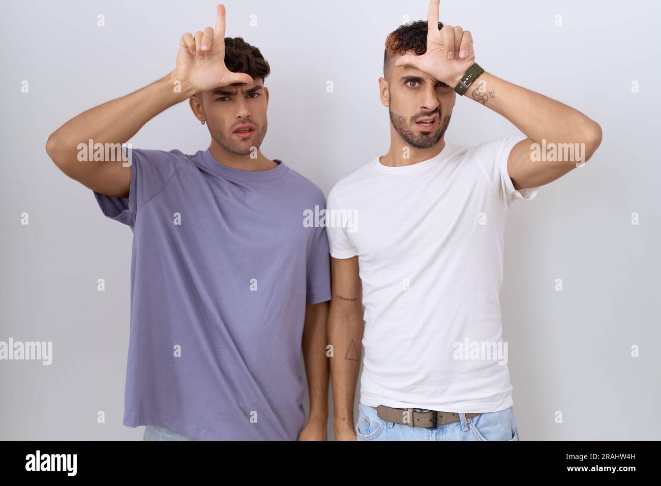 Coppia omosessuale gay in piedi su sfondo bianco che si prende gioco di  persone con le dita sulla fronte facendo gesto perdente prendendo in giro e  insultando Foto stock - Alamy