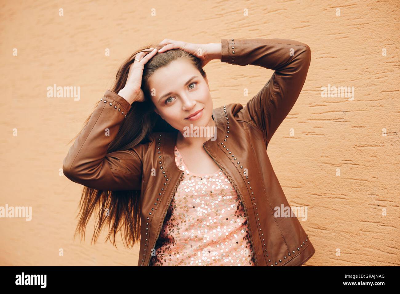Ritratto all'aperto di una giovane donna con lunghi capelli scuri, che indossa una giacca di pelle marrone Foto Stock