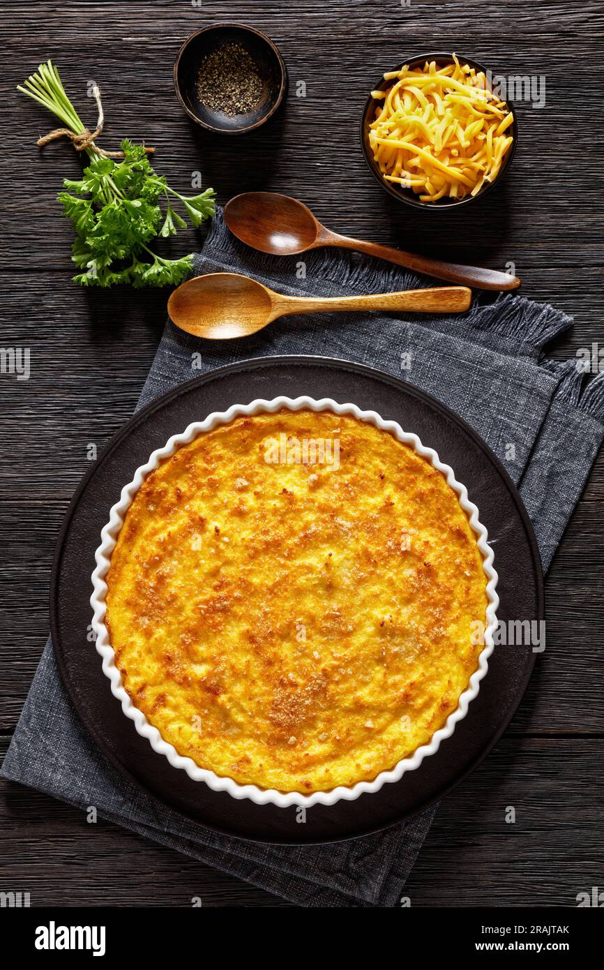 Cheddar Cheese grattugia casseruola in teglia da forno su tavolo in legno scuro con cucchiai di legno, vista verticale dall'alto Foto Stock