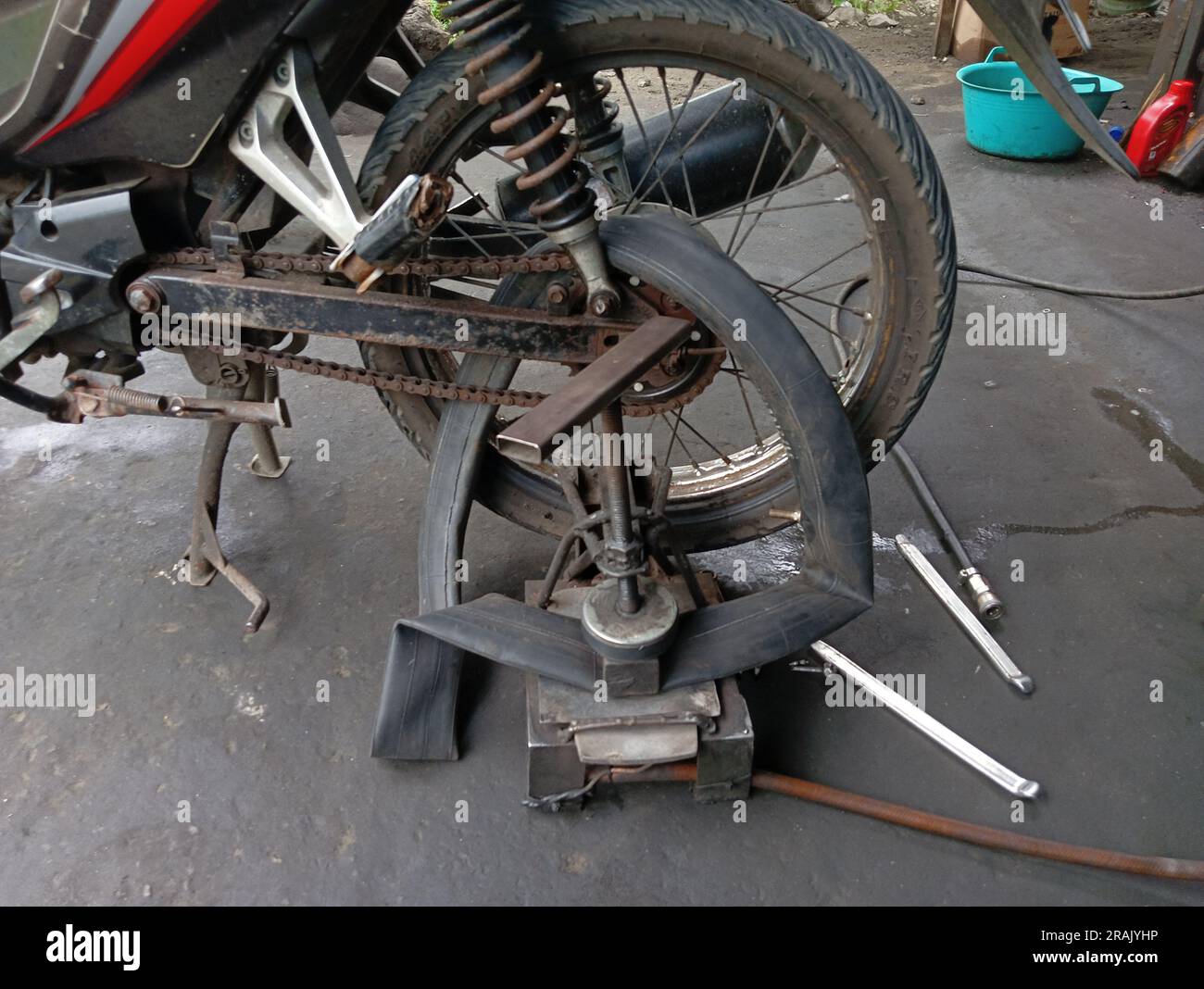 Una motocicletta il cui pneumatico posteriore viene forato e applicato con l'attrezzatura tradizionale di riparazione degli pneumatici in un'officina di riparazione. Foto Stock