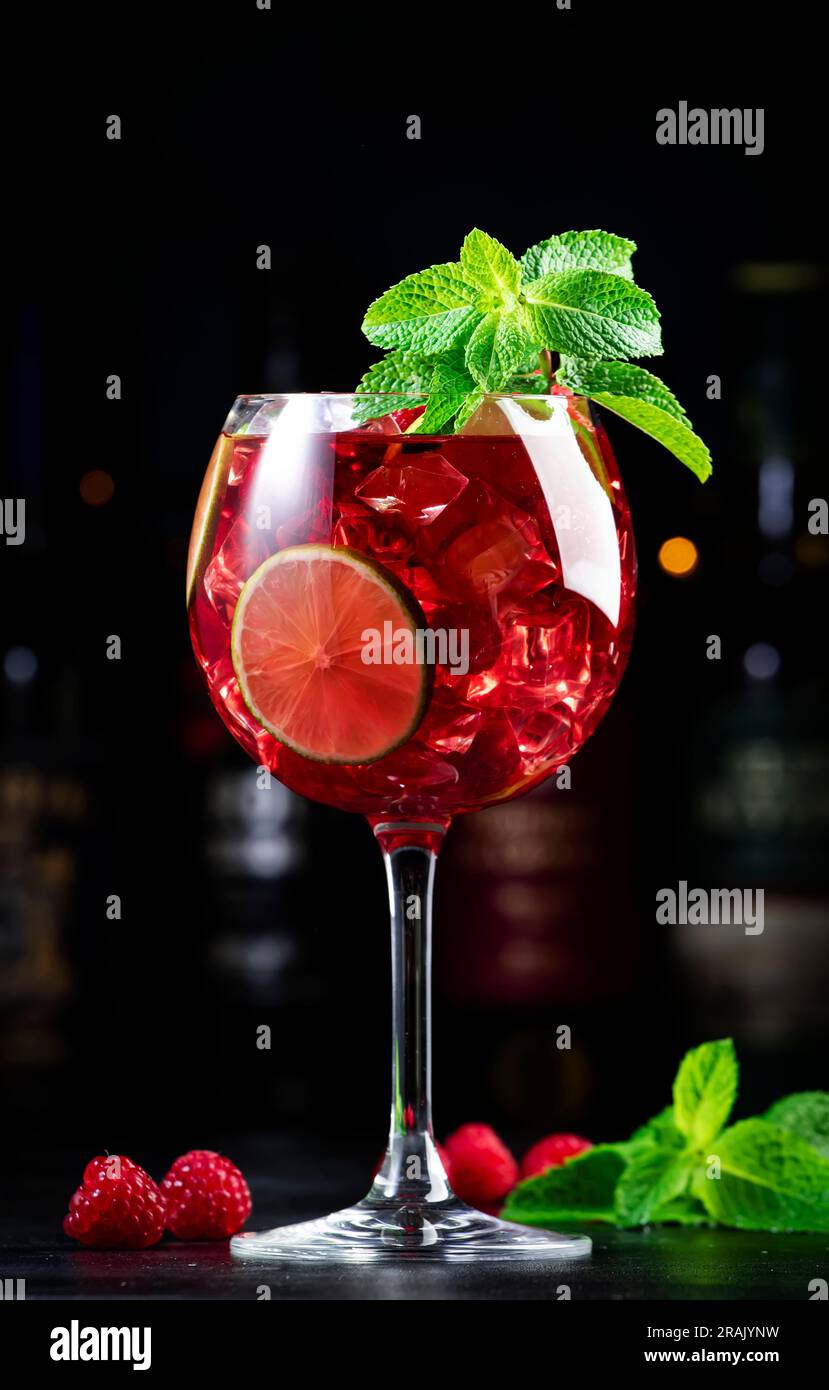 Cocktail alcolico Royal limonade con tequila, gin secco, rum bianco, vodka, liquore, lime, lamponi e ghiaccio nel bicchiere da vino. Bancone bar nero ba Foto Stock