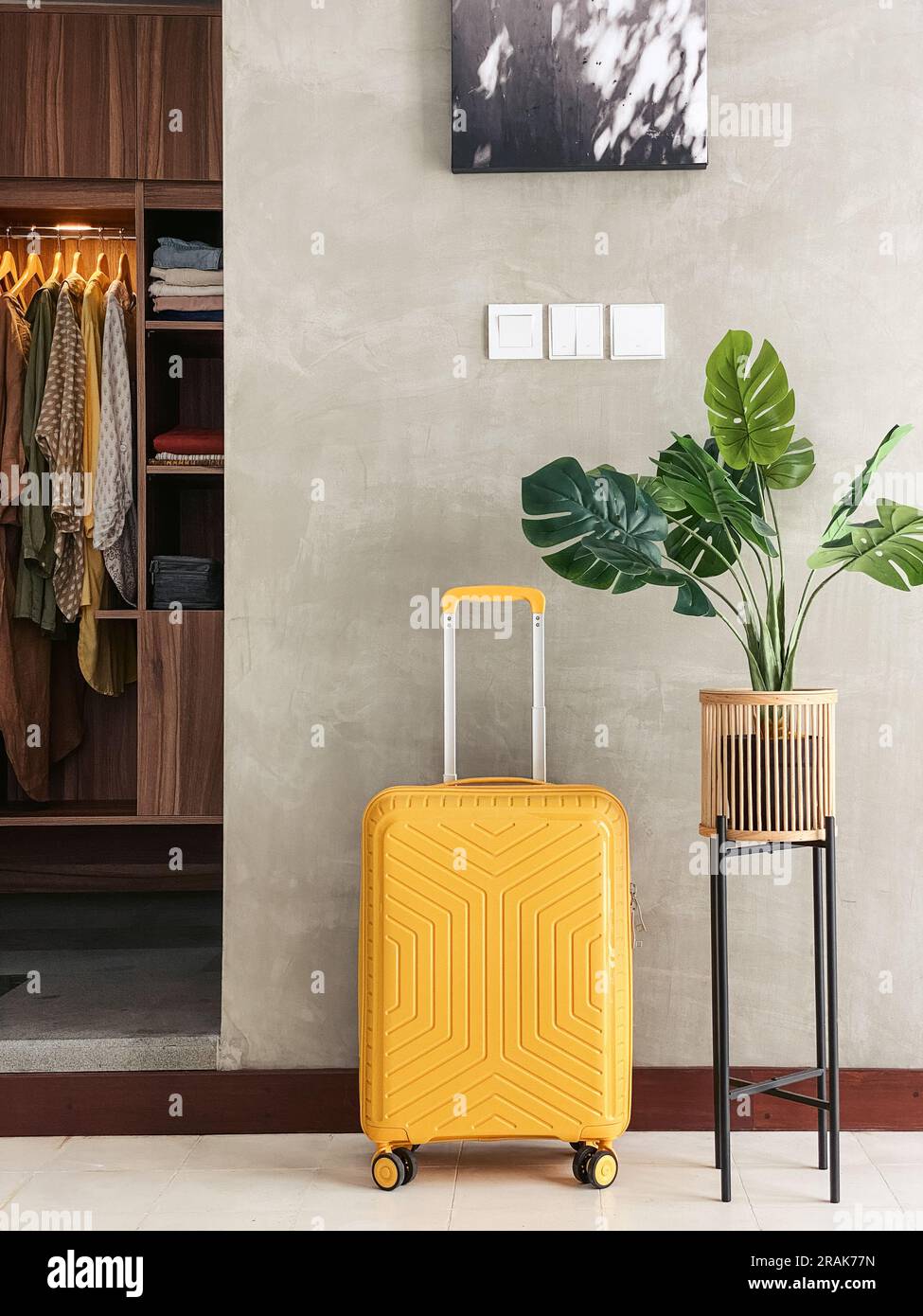 Pronto per le vacanze. Elegante valigia gialla in piedi contro la parete accanto alla monstera Foto Stock