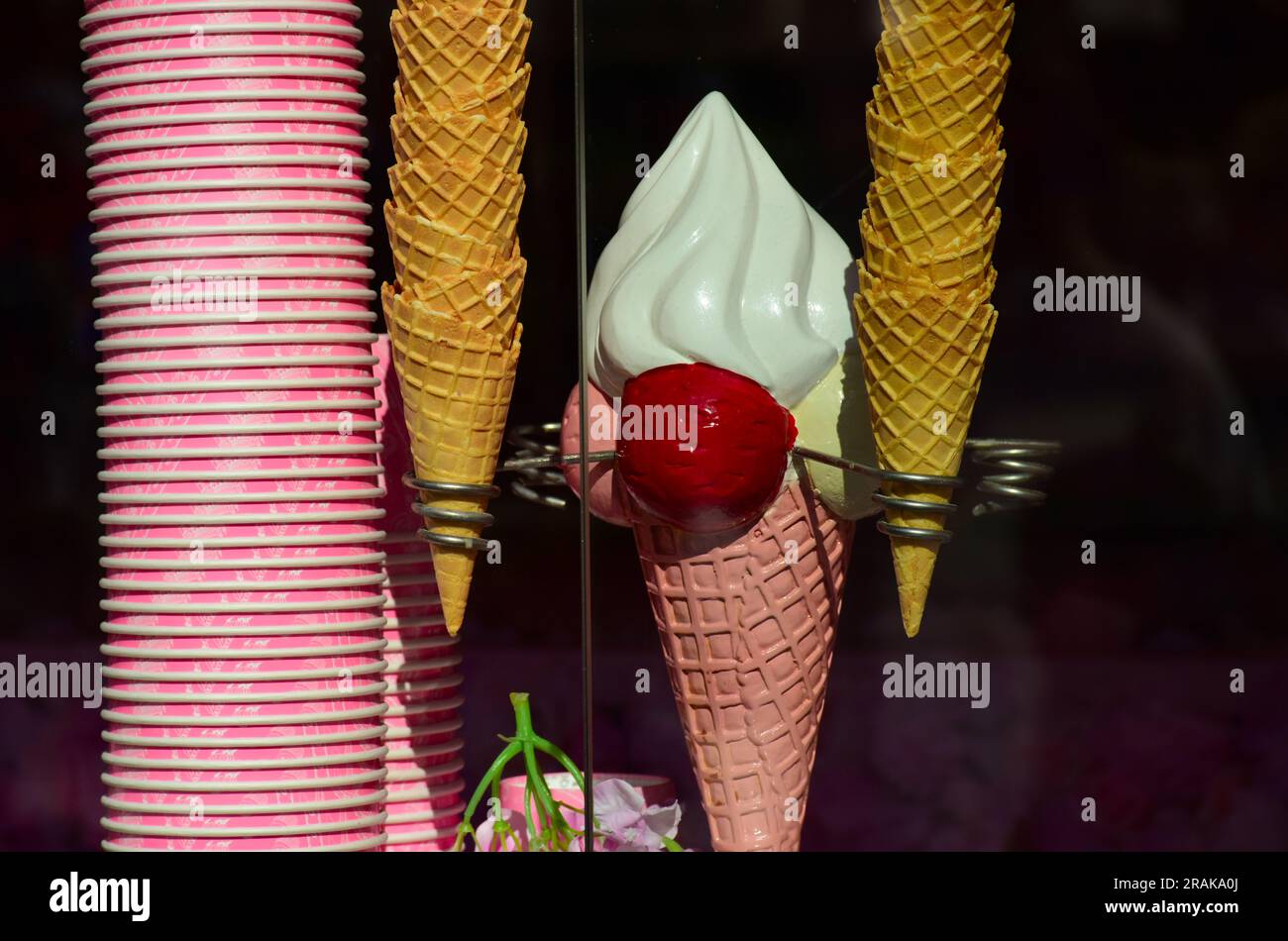tazze di carta rosa impilate per il gelato e coni di cialde morbide di colore giallo marrone esposte nella gelateria o nel venditore. decorazioni delle finestre colorate e luminose. Foto Stock