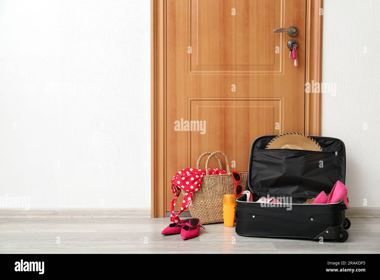 Valigia con vestiti e vimini piena di accessori da spiaggia vicino alla  porta in camera. Concetto di viaggio Foto stock - Alamy