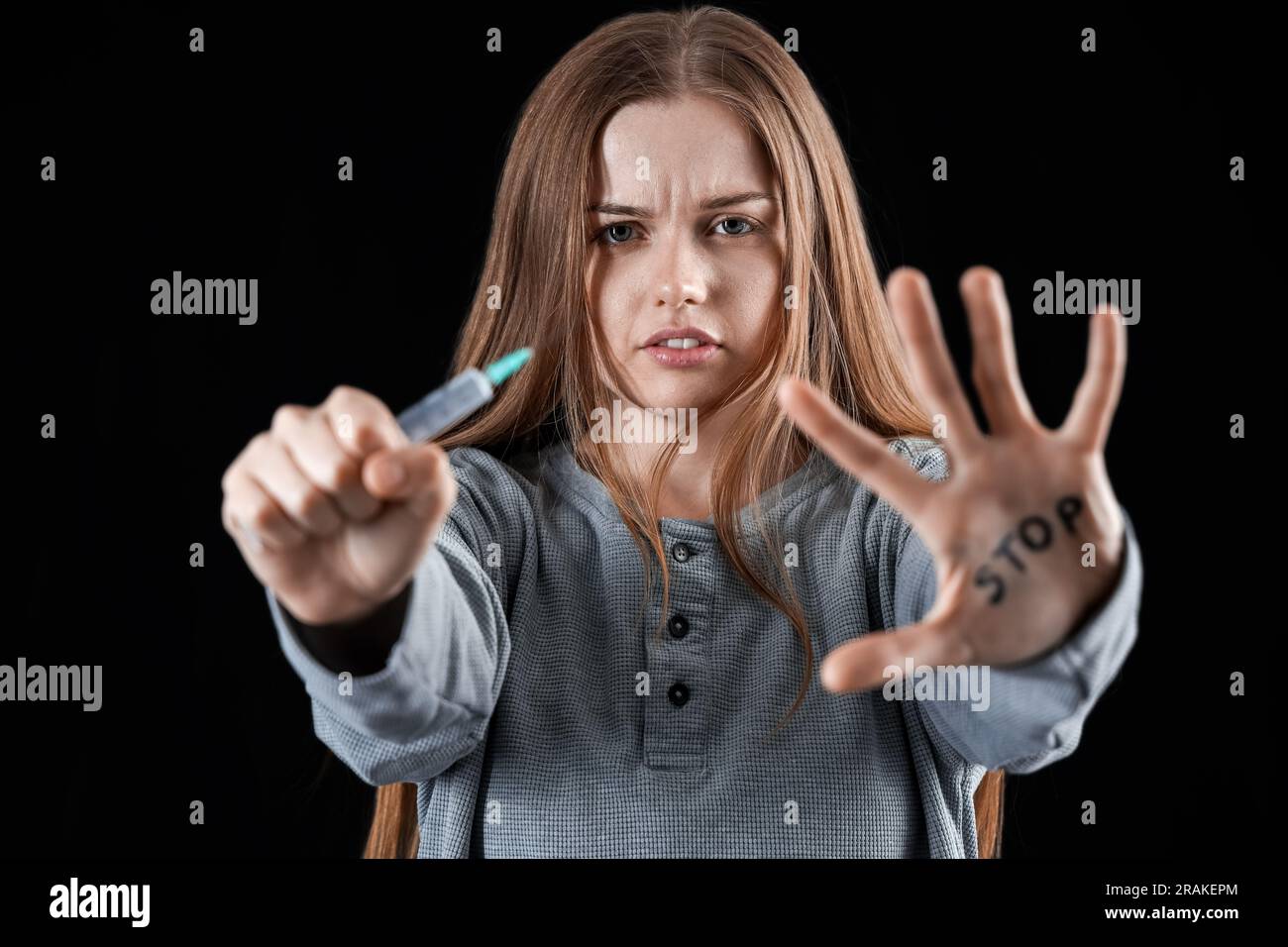 Giovane drogata con siringa e STOP DI parola scritto sul palmo su sfondo scuro Foto Stock