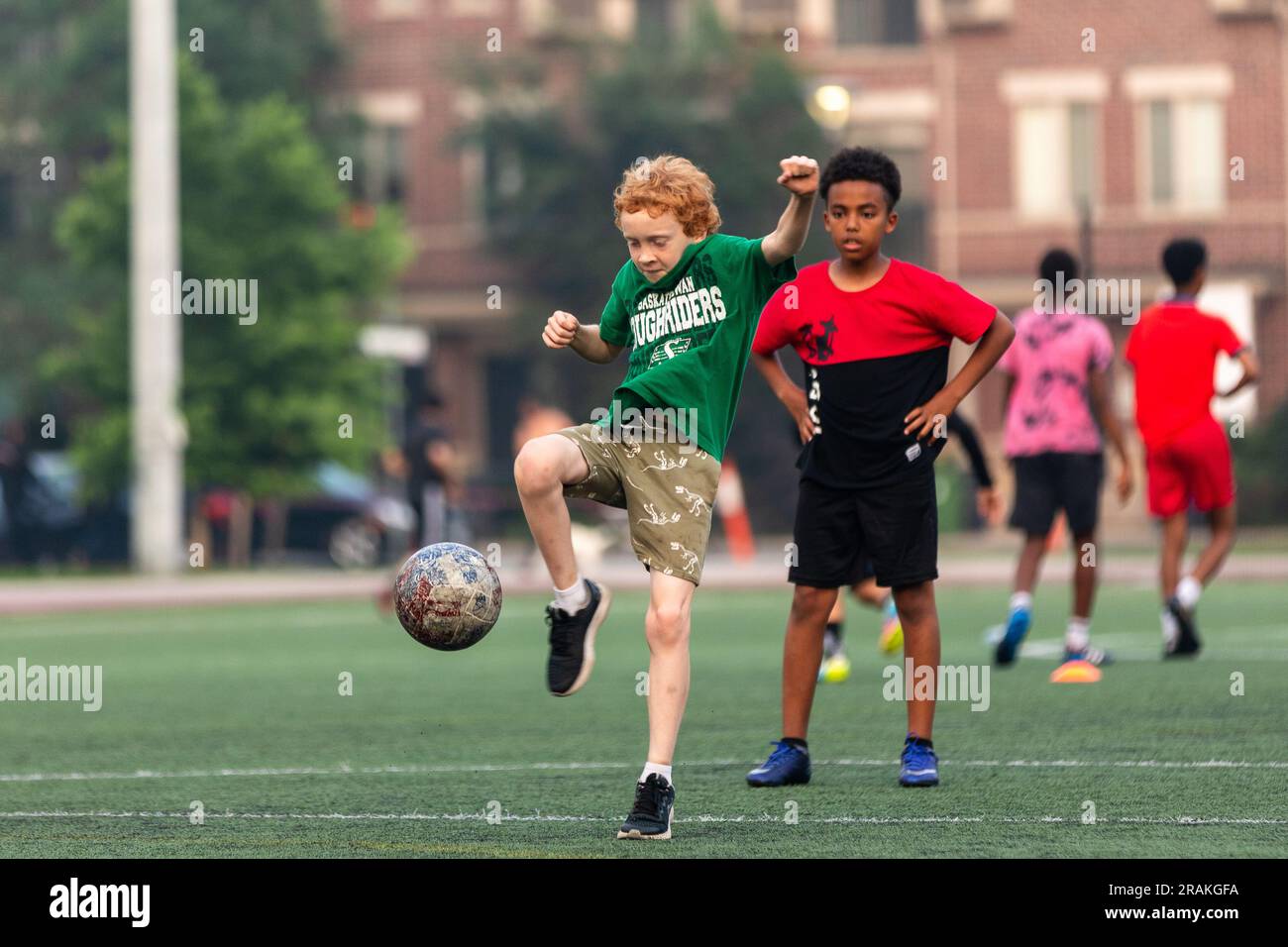 Un ragazzo pratica un calcio durante una serata estiva su un campo cittadino Foto Stock