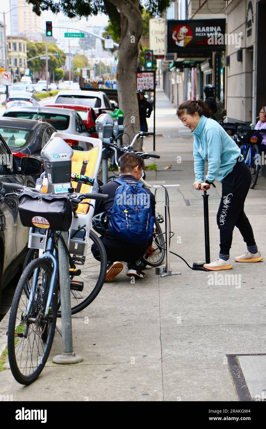 Giovane donna che gonfia una ruota per biciclette con una pompa a pavimento per biciclette ad alta pressione in una strada fuori da un'azienda di noleggio biciclette San Francisco California USA Foto Stock