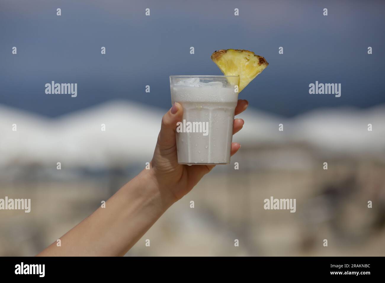 Mano di donna con cocktail Pina colada con spiaggia dietro Foto Stock
