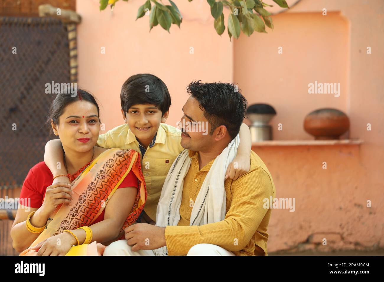 Ritratto della famiglia contadina indiana di padre, madre e figlio seduti insieme su una culla in abito da abitante indiano. Foto Stock