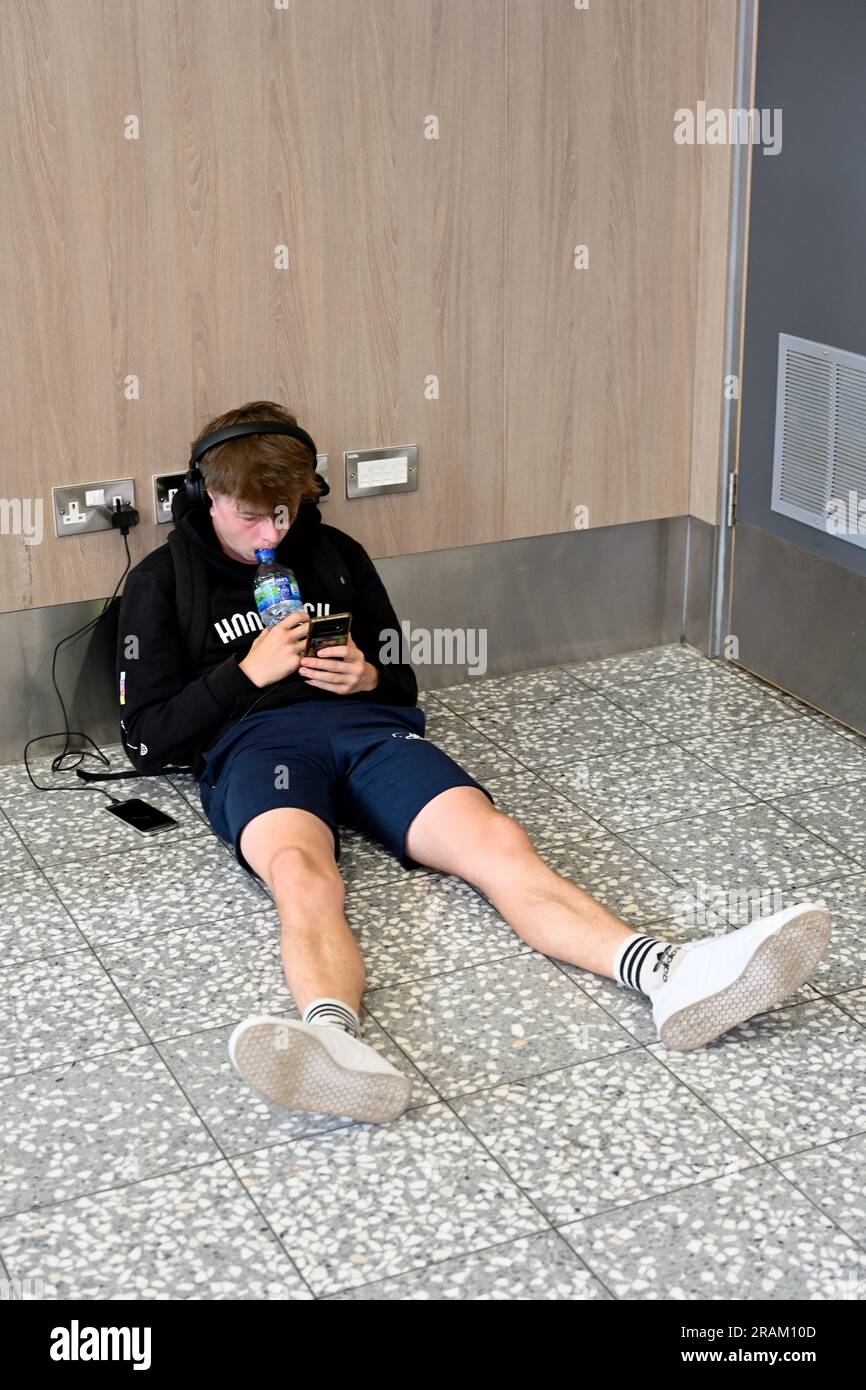 Seduto sul telefono di ricarica a pavimento collegato alla presa di alimentazione, Regno Unito Foto Stock