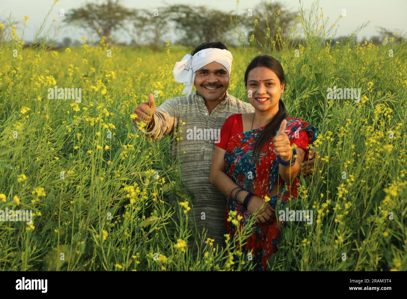 Felice coppia di agricoltori indiani in piedi in un campo di senape che si gode dei profitti agricoli e felice di vedere i benefici delle coltivazioni agricole. Foto Stock