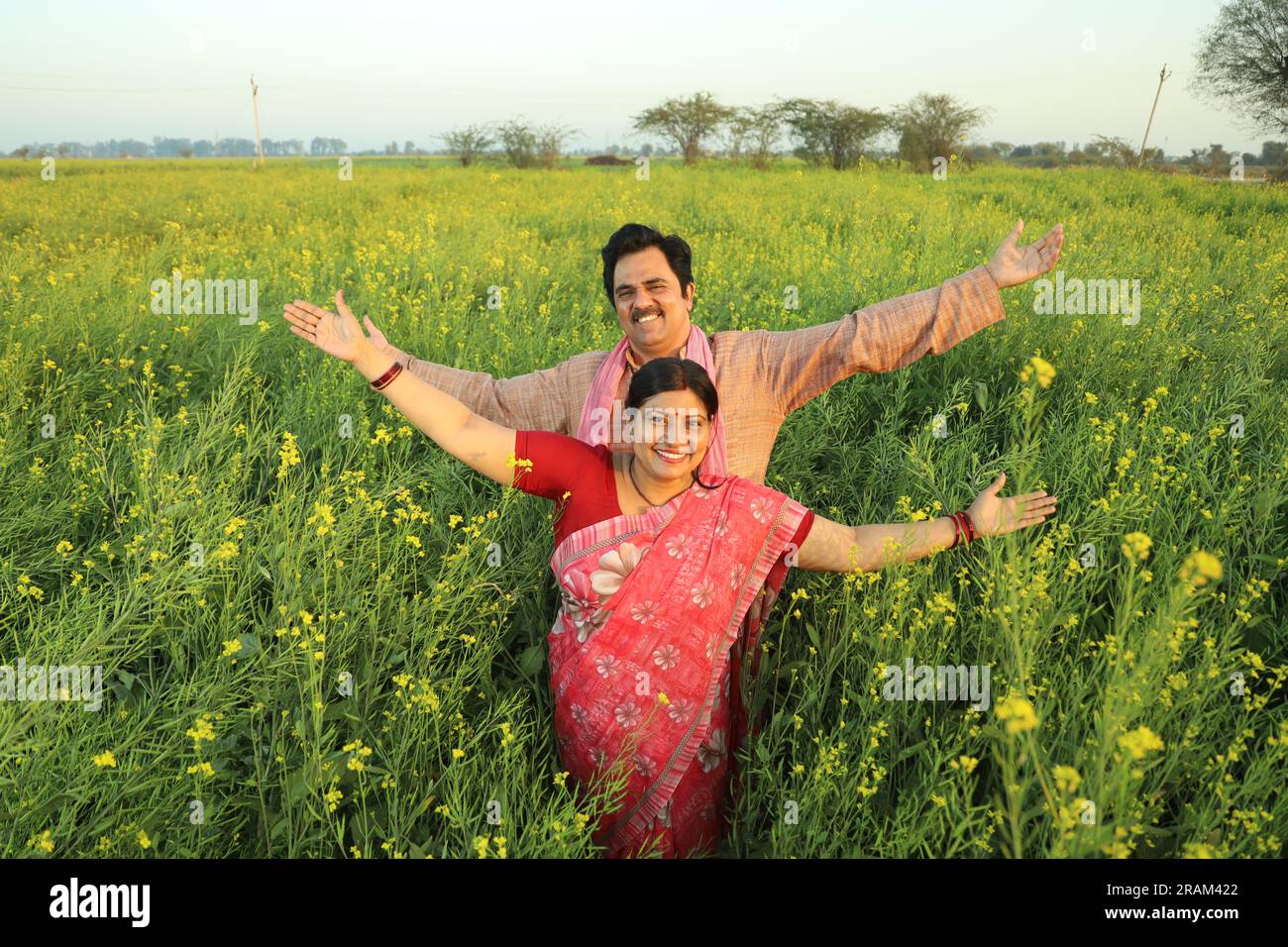 Felice coppia di agricoltori indiani in piedi in un campo di senape che si gode dei profitti agricoli e felice di vedere i benefici delle coltivazioni agricole. Foto Stock