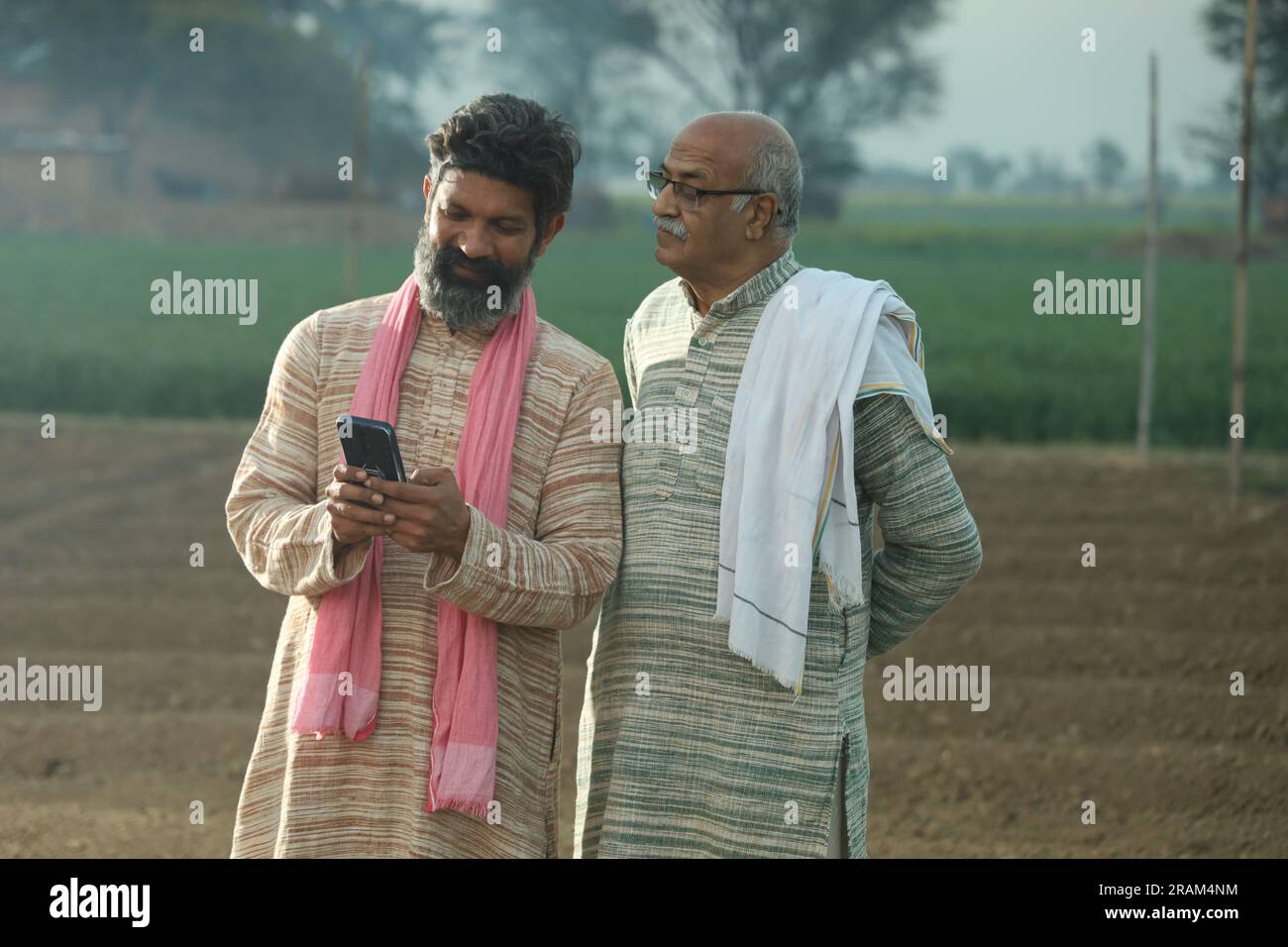 Bella composizione di due contadini indiani in piedi nel campo. Concetto agricolo che ritrae gli agricoltori al lavoro guardando lo smartphone. Foto Stock