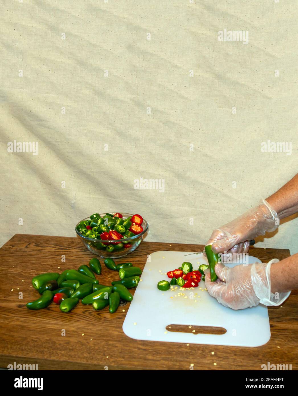 Indossando guanti di plastica, l'addetto alla cucina tiene il pepe jalapeno e lo taglia con attenzione. Foto Stock