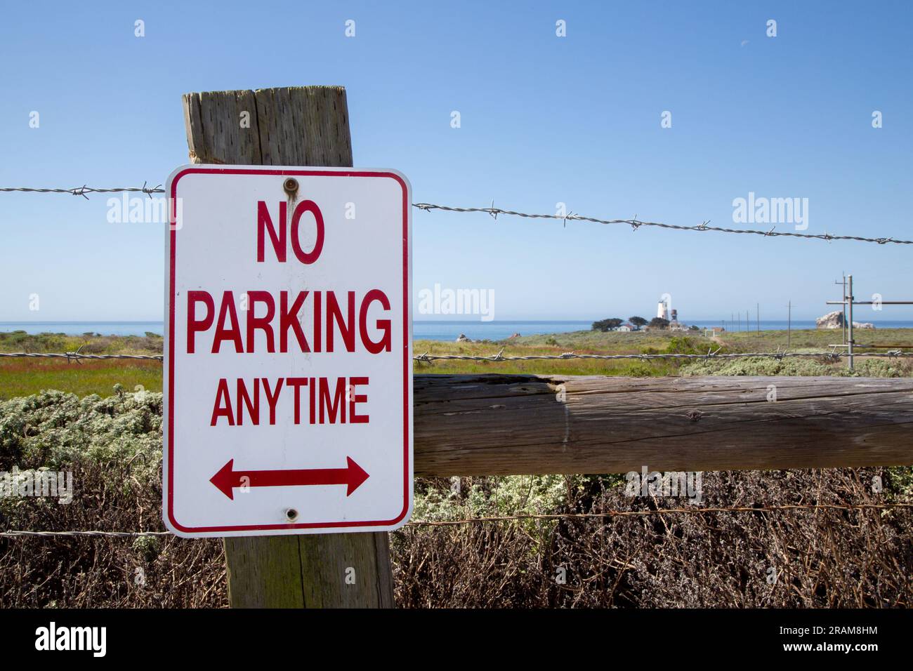 Non è consentito parcheggiare in qualsiasi momento sulla recinzione con filo spinato. Non è consentito parcheggiare in qualsiasi momento con il faro di fronte all'oceano sullo sfondo. Nessun cartello per il parcheggio in America su un percorso turistico Foto Stock