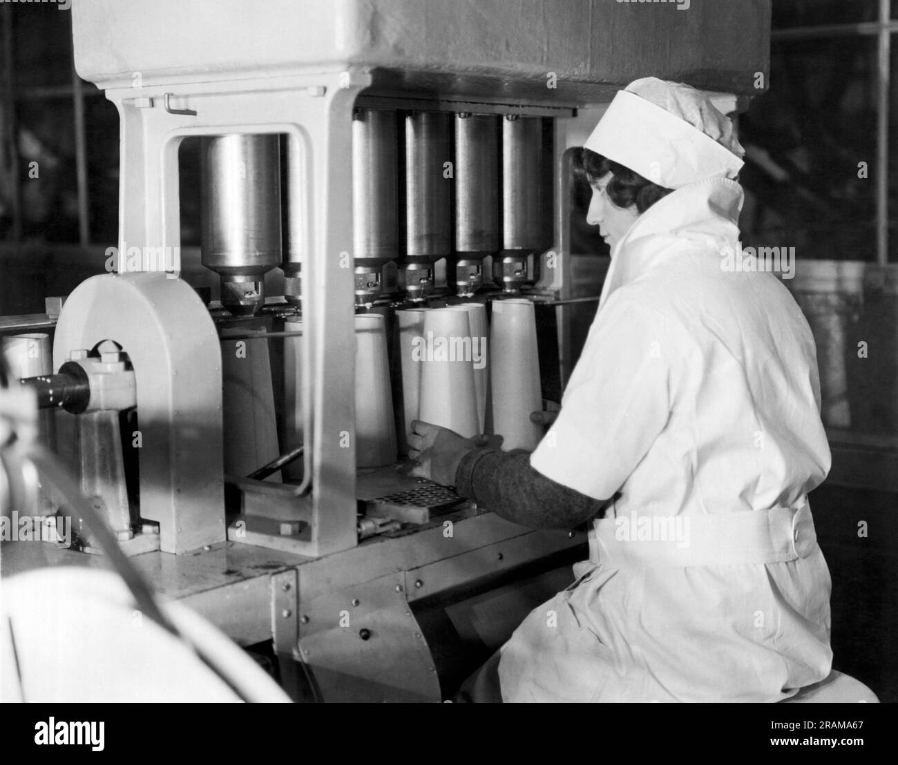 New York, New York: c. 1928 lavoratori di Sheffield Dairy Farms che utilizzano i nuovi contenitori di carta Sealcone in cui imballare il latte, sostituendo la bottiglia di vetro. Sono più leggeri, non si rompono e confezionano il doppio dell'efficienza grazie alla loro forma conica. Qui, dopo che i contenitori conici sono stati rivestiti con paraffina, vengono riempiti con precisione dalla macchina. Foto Stock