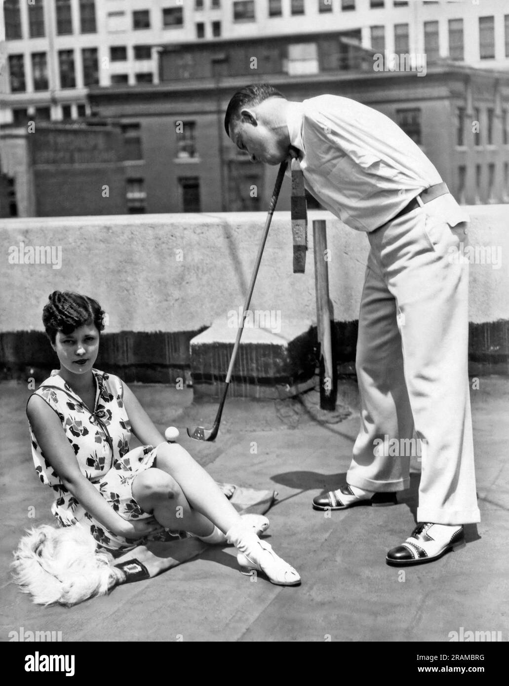 Los Angeles, California: c. 1930. Thomas McAuliffe, un mago di golf senza braccio, esegue una acrobazia incredibile. Tenendo la mazza tra collo e spalla, guida la palla da golf a 175 metri dalla ginocchia di una donna. Foto Stock