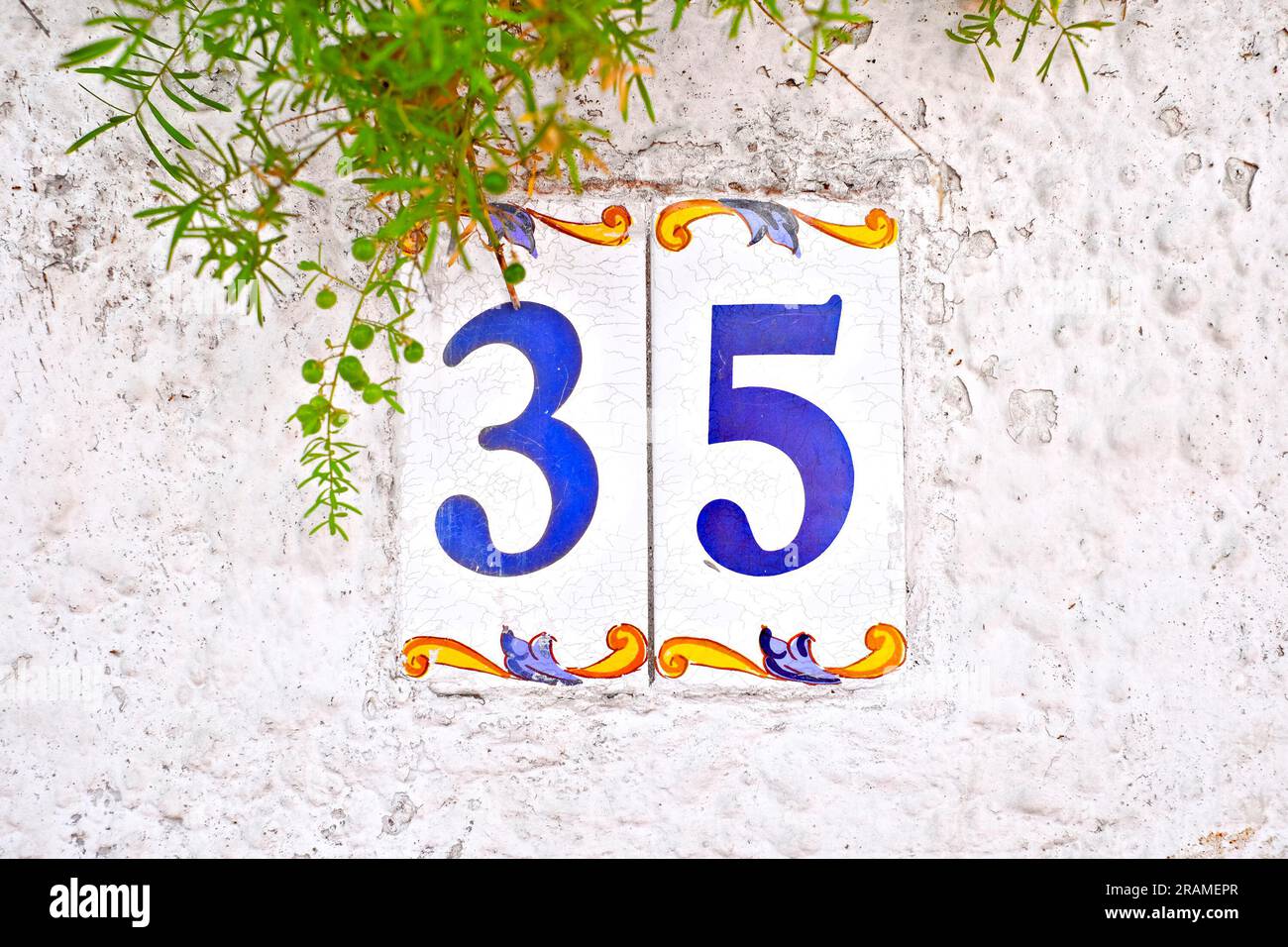 Trentacinque, numero 35, piastrelle numerate decorative con elemento floreale su parete bianca. Foto Stock