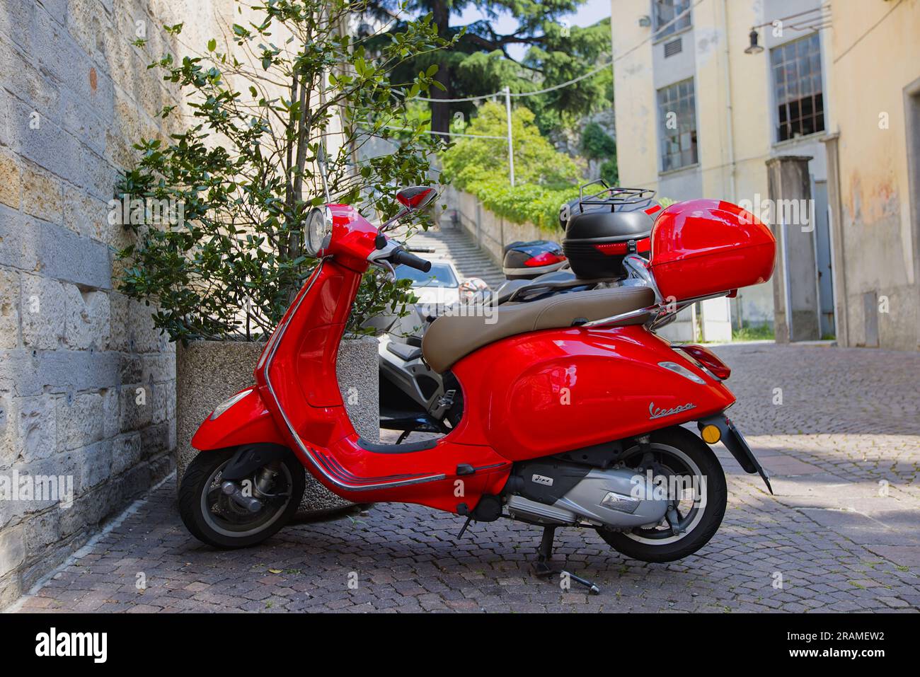 Una Vespa rossa parcheggiata di fronte a una chiesa nella città di Belano, nell'Italia settentrionale. Soleggiata giornata di giugno. Foto Stock