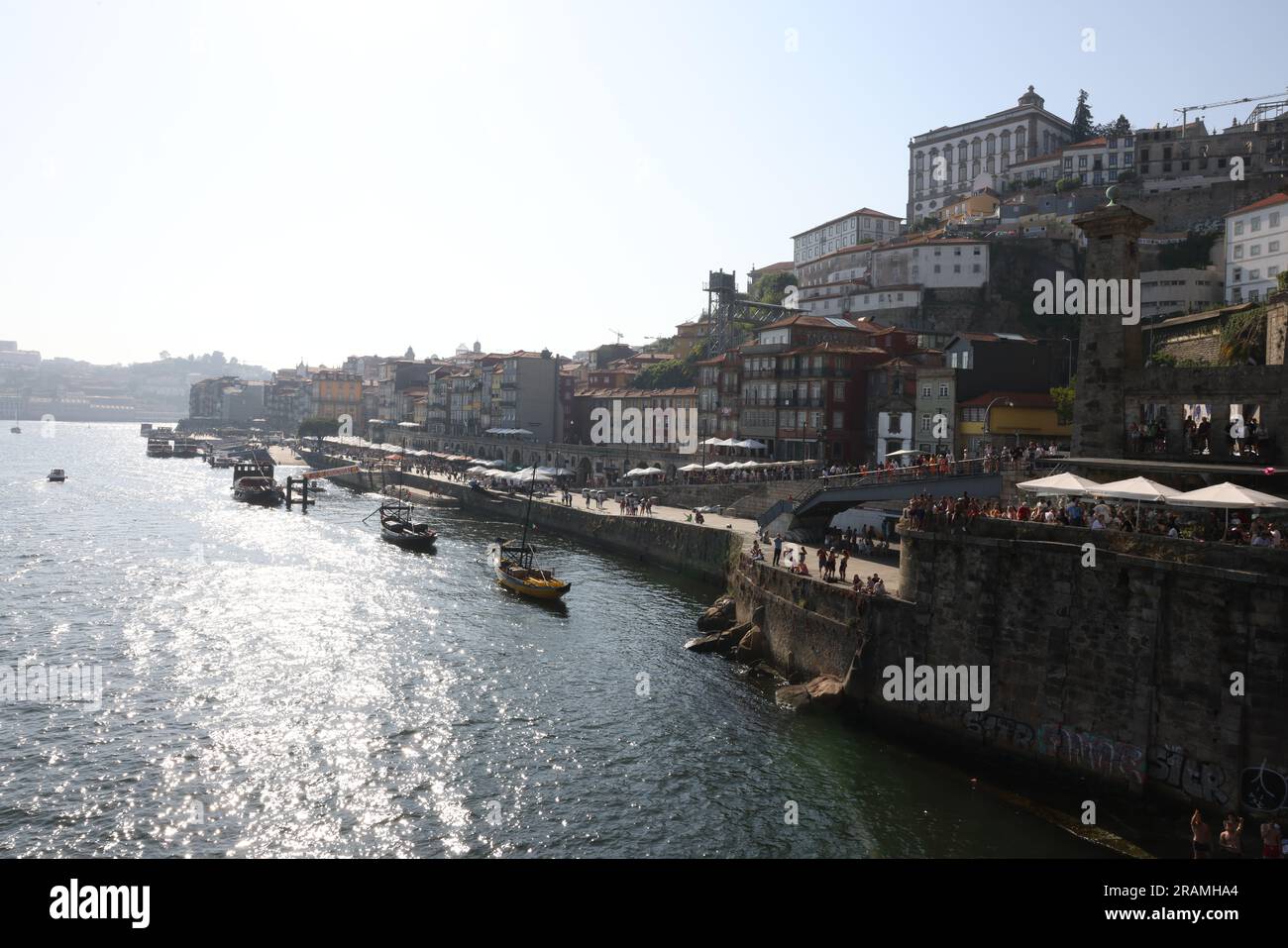 Un tramonto che si affaccia sulla città di Porto mentre la gente si siede sul bordo dell'acqua e altri saltano nel fiume Duoro per una nuotata serale. Foto Stock