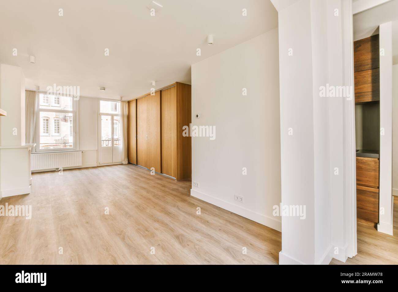 un soggiorno vuoto con pavimento in legno e grandi finestre nella camera sono pareti bianche, pavimenti in legno duro e porte in legno Foto Stock