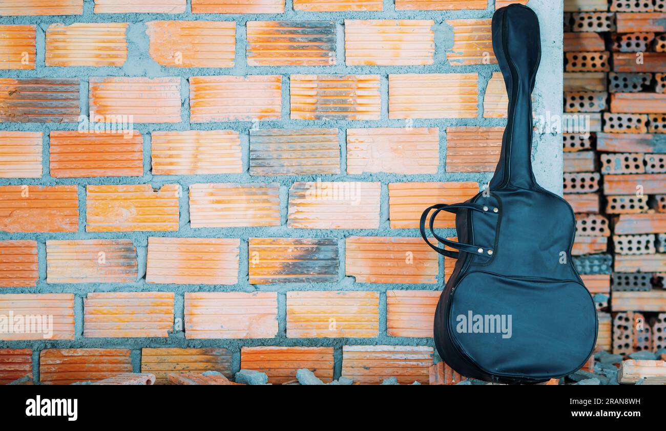 All'interno della casa - custodia nera per chitarra acustica, sfondo marrone muro di mattoni. Foto Stock