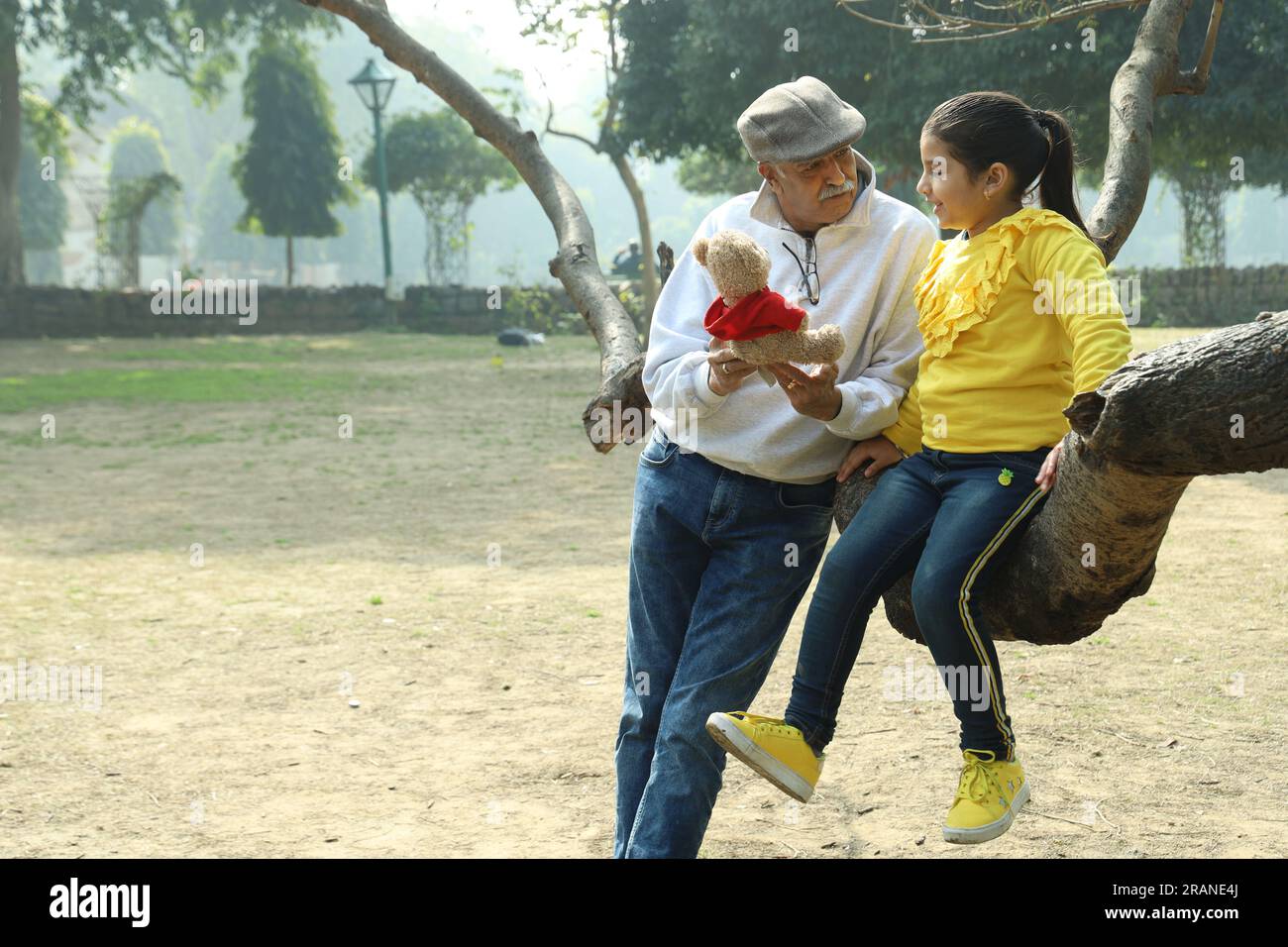 Nonno che si diverte con la nipote nel parco circondato da verde e serenità. Stanno trascorrendo un momento gioioso e allegro insieme Foto Stock