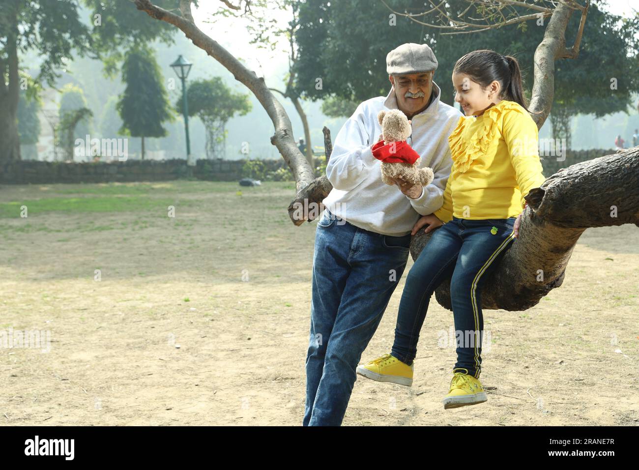 Nonno che si diverte con la nipote nel parco circondato da verde e serenità. Stanno trascorrendo un momento gioioso e allegro insieme Foto Stock