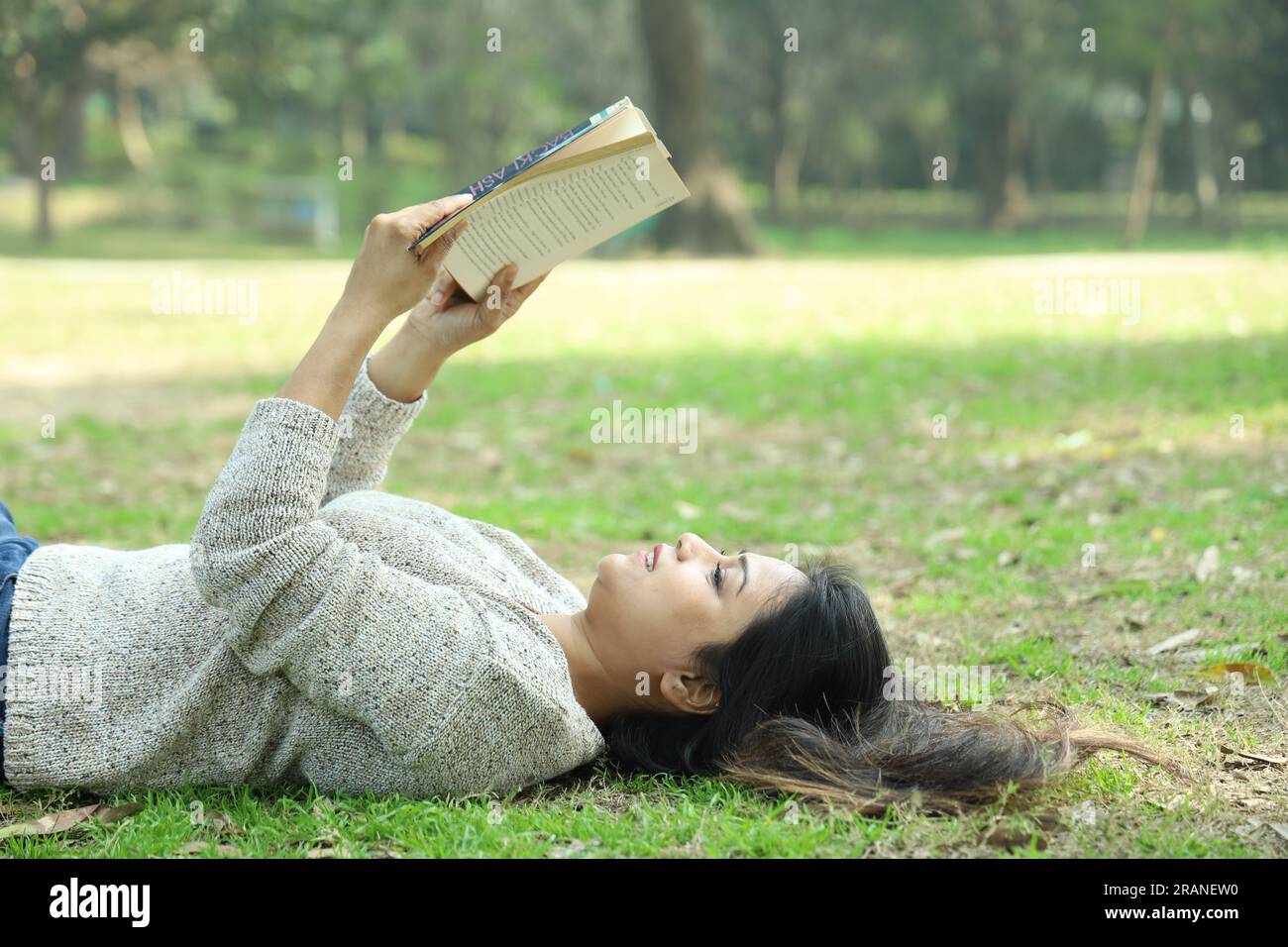 Una bella ragazza universitaria che legge un libro sdraiato nell'erba tra un giorno. Ambiente verde e tranquillo Foto Stock