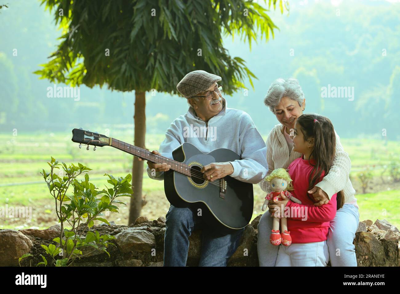 Felice vecchia coppia seduto insieme nel parco verde. Il nonno esegue canzoni suonando la chitarra e godendosi l'esibizione in serenità e tranquillità. Foto Stock