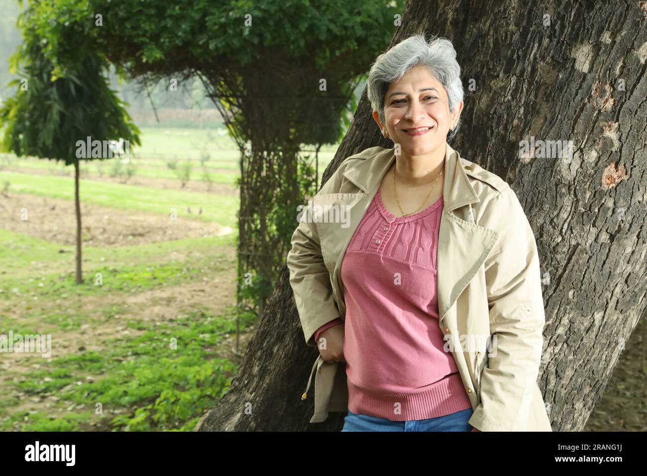 Ritratto di una donna dai capelli grigi di mezza età in piedi sotto gli alberi nel parco circondato da un ambiente sereno e aria pulita. Foto Stock