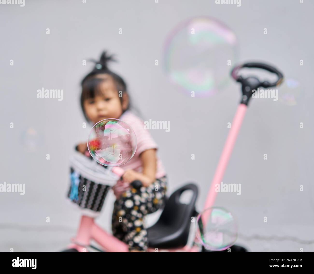 Una bolla che galleggia di fronte a un bimbo sfocato, su una bicicletta, il tempo del concept è breve. Foto Stock