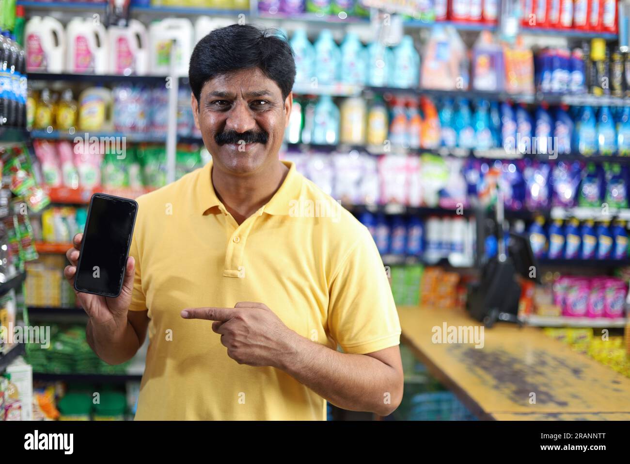 Uomo sorridente di mezza età che acquista in un negozio di alimentari e punta verso l'app mobile. Acquisto di generi alimentari in un supermercato che punta verso l'app mobile. Foto Stock