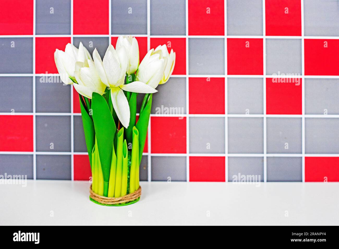 bouquet di tulipani bianchi sul tavolo sullo sfondo di una parete a scacchi rosso-grigio. Atmosfera natalizia Foto Stock