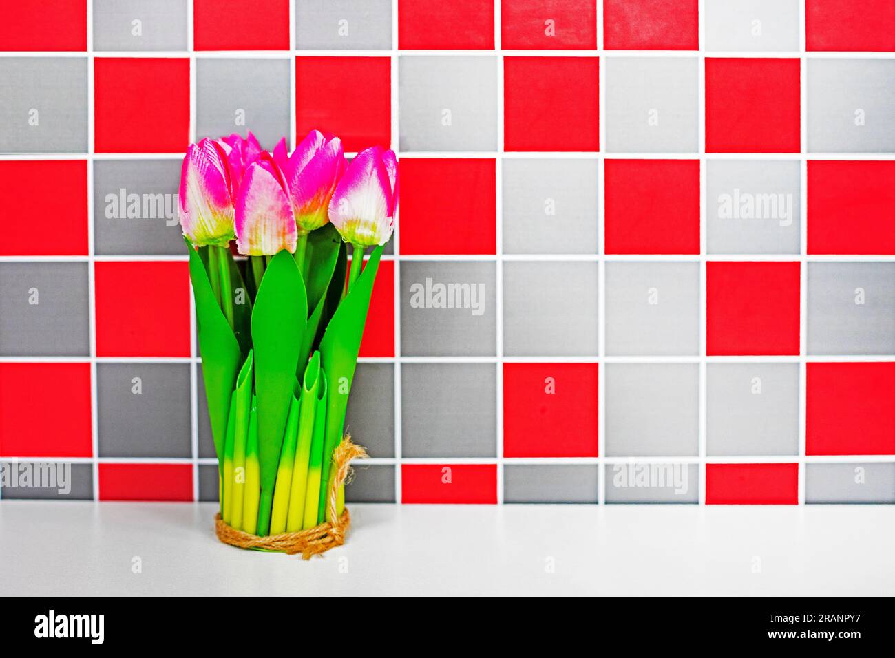 bouquet di tulipani rosa sul tavolo sullo sfondo di una parete a scacchi rosso-grigio. Atmosfera natalizia Foto Stock