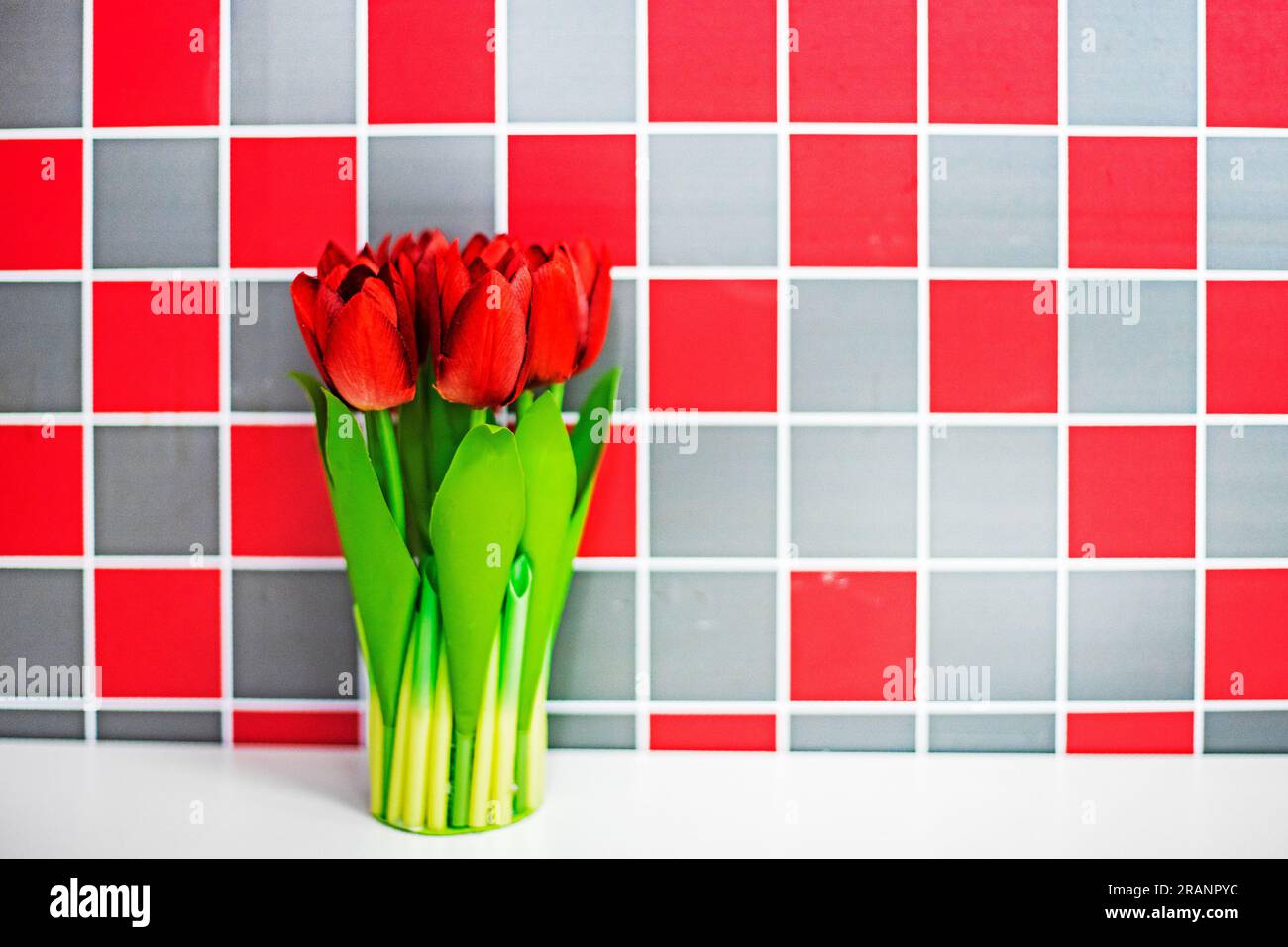 bouquet di tulipani rossi in un bicchiere su un tavolo bianco in . Atmosfera natalizia. congratulazioni Foto Stock