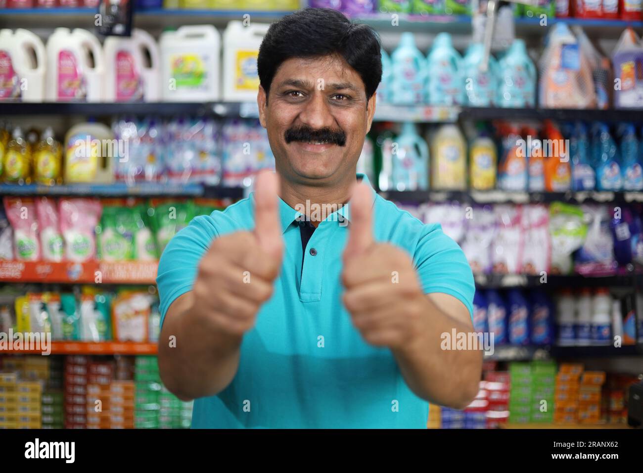 Sorridente indiano di mezza età che acquista in un negozio di alimentari. Comprare della spesa per casa in un supermercato. Uomo allegro e gioioso che fa il pollice in alto. Foto Stock