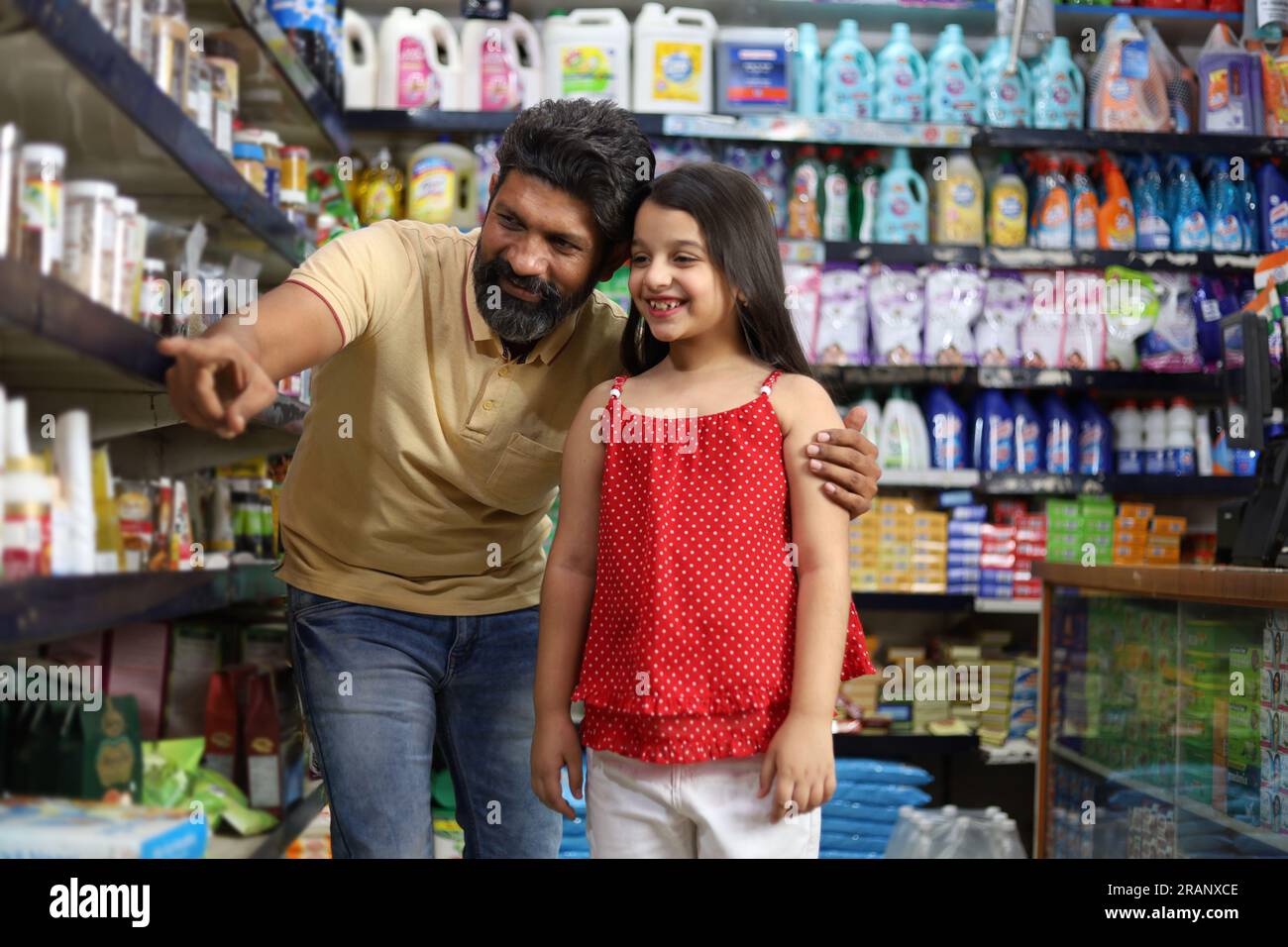 Padre felice con una figlia che acquista in un negozio di alimentari. Comprare della spesa per la casa al supermercato. Rivolto verso lo scaffale del prodotto. Esigenze quotidiane. FMCG. Foto Stock