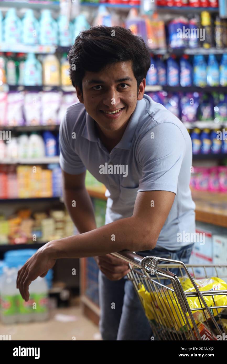 Bellissimo ritratto di bel giovane indiano sorridente che fa shopping e posa nell'ipermercato. Mini centro commerciale locale sorrisi felici di clienti soddisfatti. Foto Stock