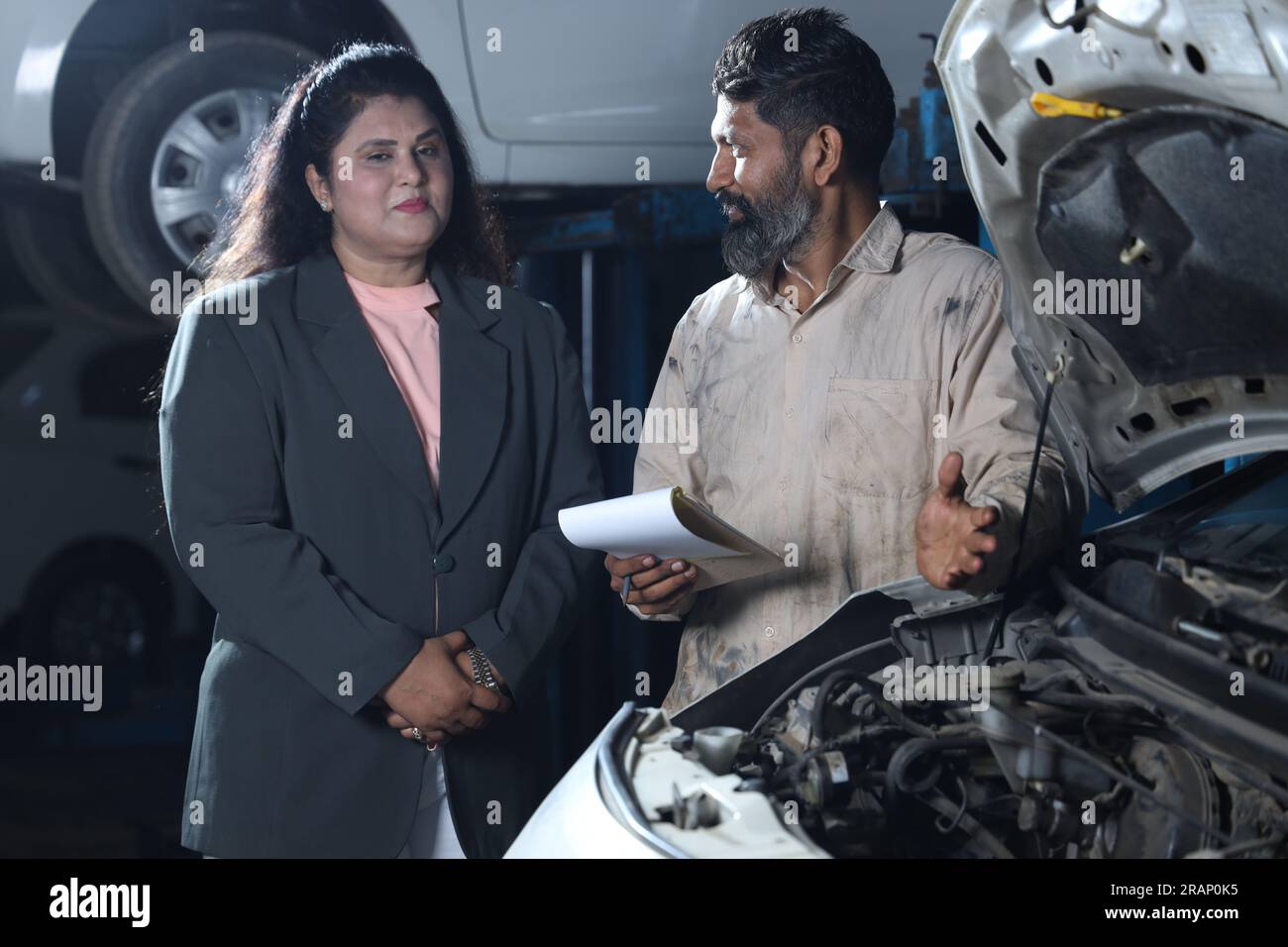 Meccanico in piedi con cliente felice che stringe la mano. Il cliente è soddisfatto di ottenere la consegna in tempo. Rapporto completo sull'auto in mano. Foto Stock