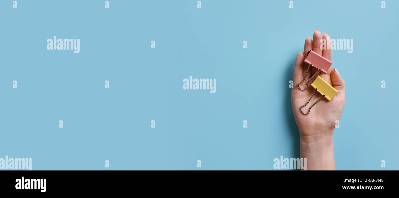 Mano femmina con clip per rilegatura per carta su sfondo azzurro con spazio per il testo Foto Stock