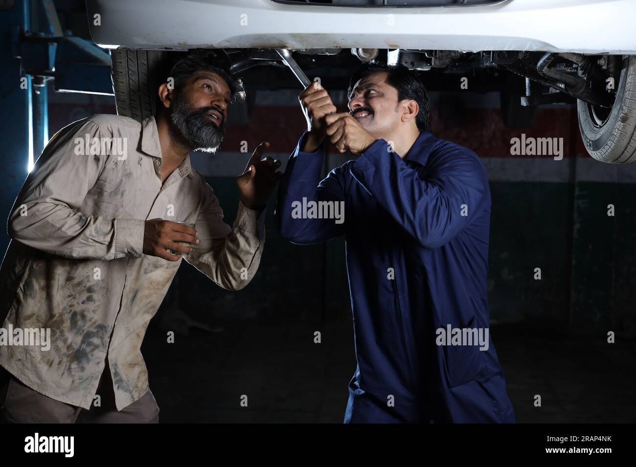 Meccanici in piedi e che lavorano insieme nella stazione di servizio. Specialisti che esaminano l'auto sollevata. Riparatori professionisti che parlano, fanno prestazioni. Foto Stock