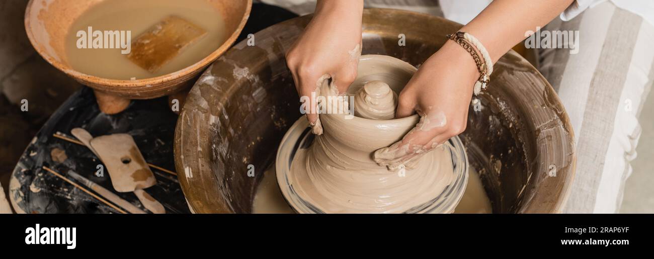 Vista ad alto angolo di una giovane donna di vasaio che forma l'argilla umida mentre lavora con la ruota e la ciotola in ceramica con acqua e spugna in un laboratorio di ceramica, ceramiche S. Foto Stock