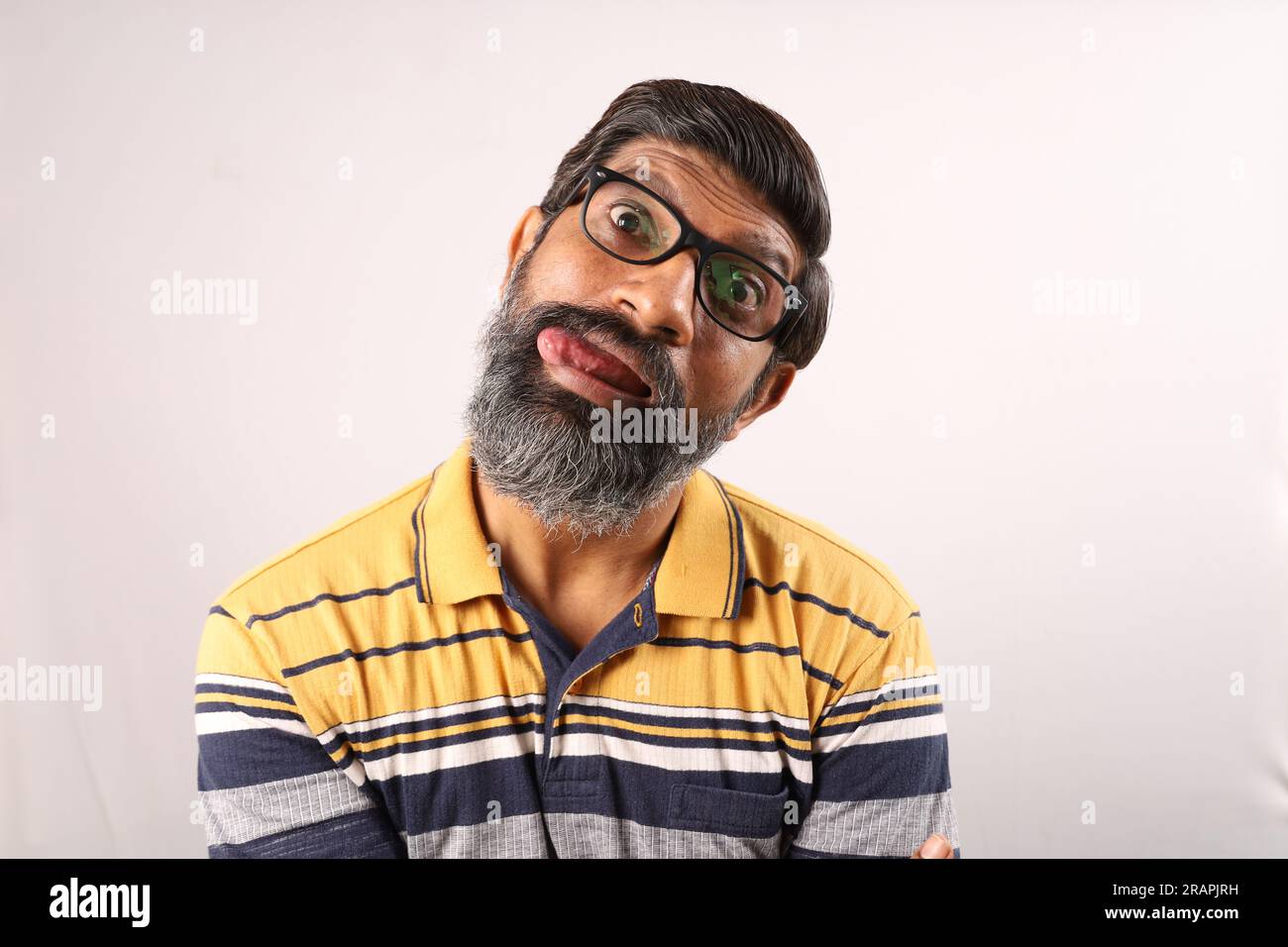 Ritratto di un uomo indiano barbuto che indossa occhiali e t-shirt. Espressioni funky volto distorto. Uomo sbalordito che mostra vari stati d'animo di stravagante personalità. Foto Stock