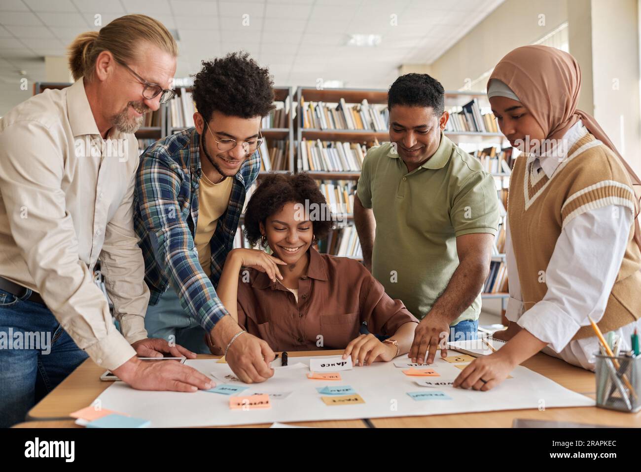 Gruppo di studenti migranti che imparano le parole inglesi insieme all'insegnante a tavola durante la lezione Foto Stock