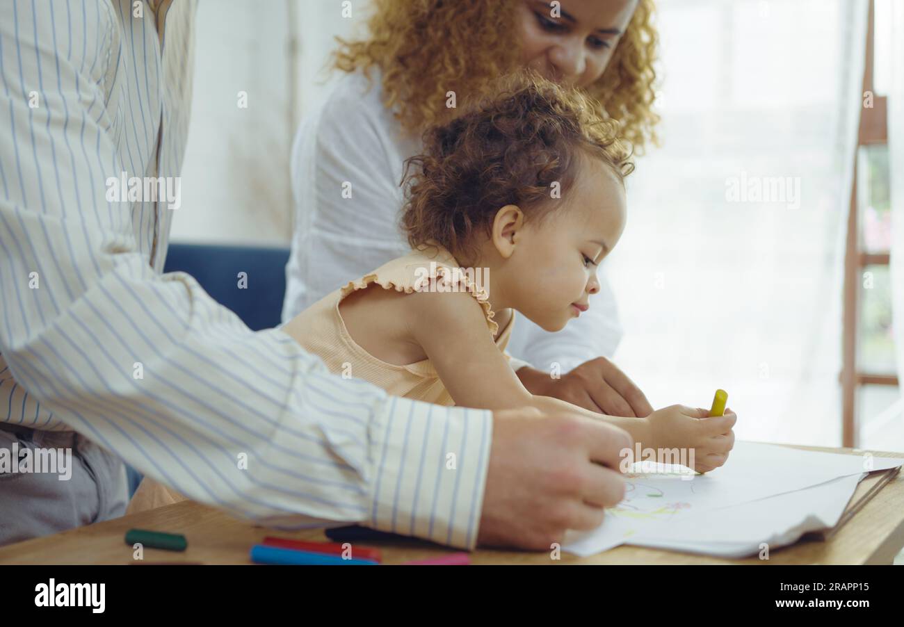 Papà, mamma e figlia piccola disegnano con matite colorate su carta sorridente.i giovani trascorrono del tempo libero insieme in salotto a casa. Foto Stock