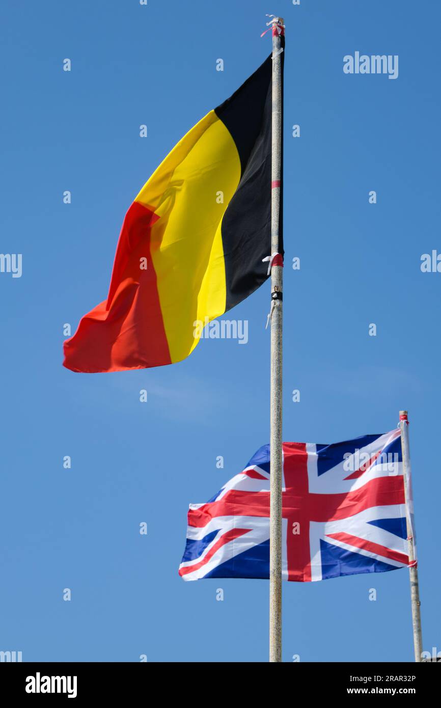 In primo piano la bandiera belga e sullo sfondo la bandiera inglese che sventola in un cielo limpido. Foto Stock